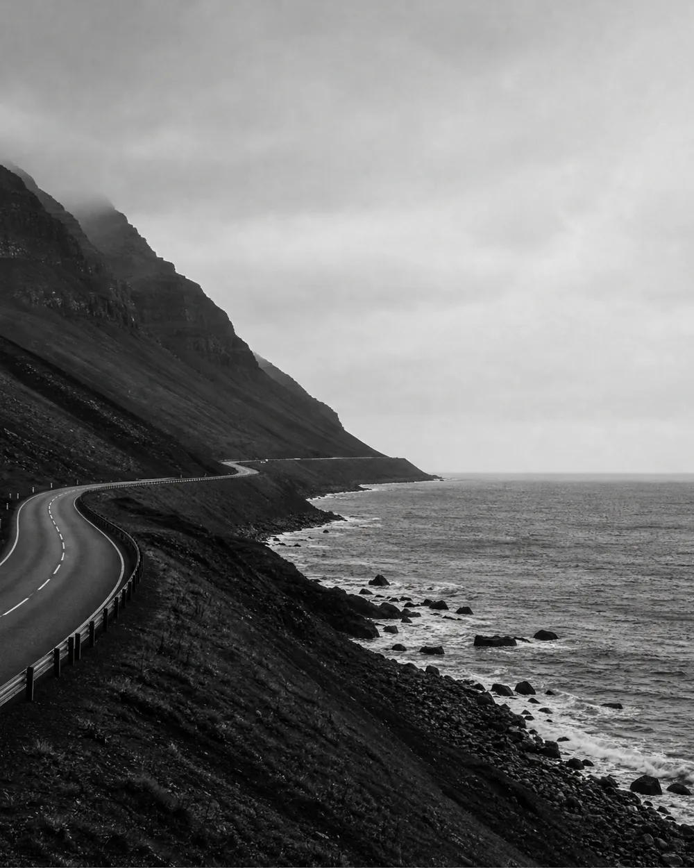 An empty road running into mountains under heavy cloud.