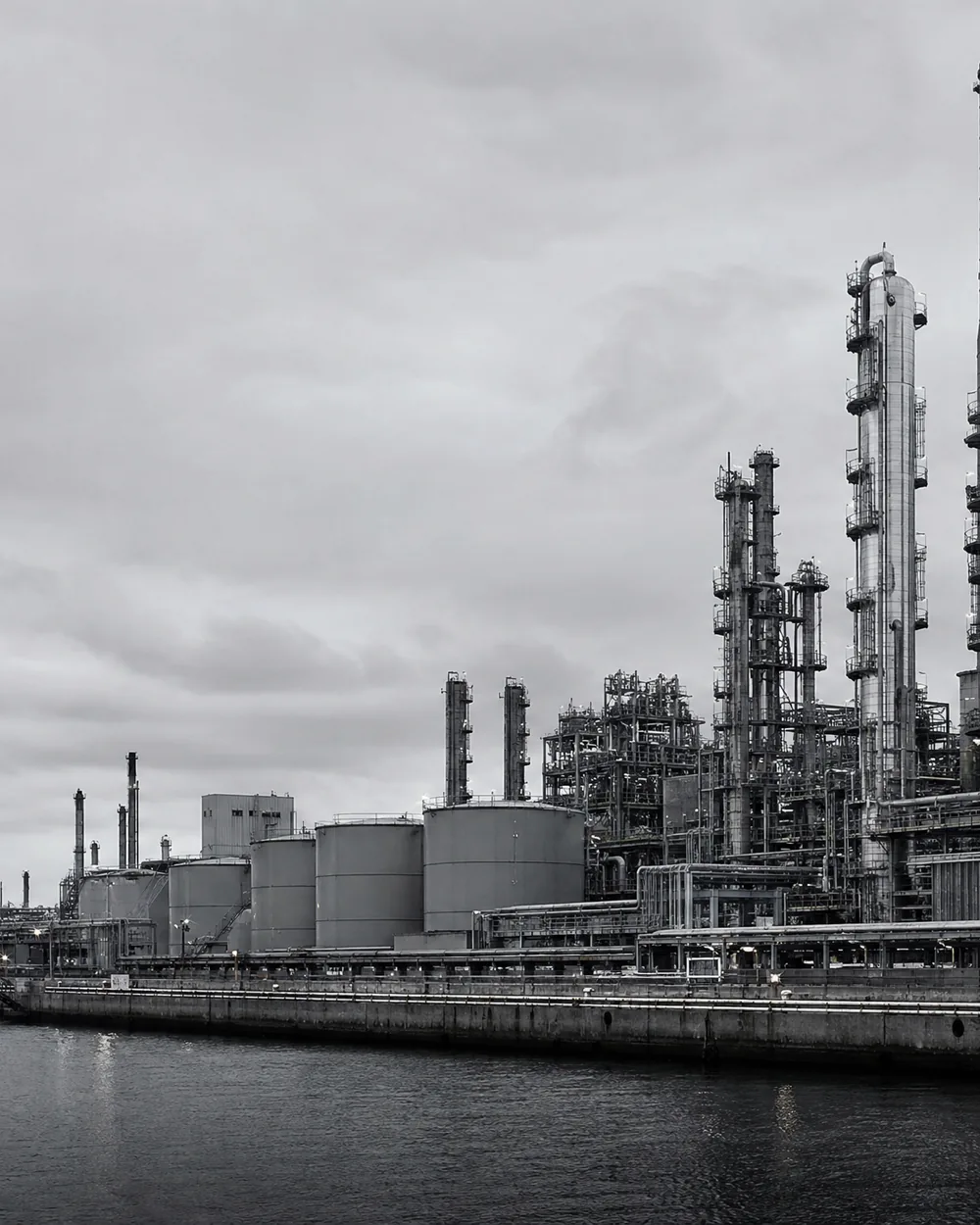 An industrial plant of towers and pipework under flat grey light.